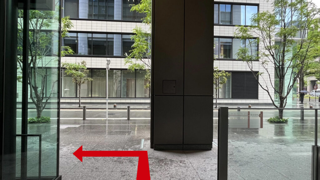 地上出口から外に出た直後の景色。正面にグレーのビルが見え、足元はタイル貼りになっている。