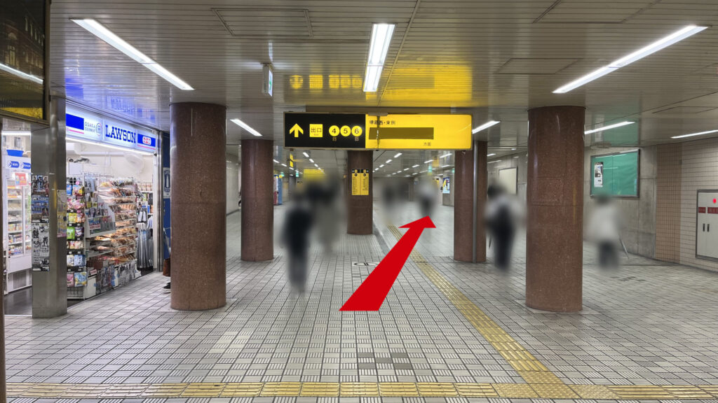 エスカレーターを上がった風景 左にローソン、正面に4、5、6号出口の黄色と黒の案内看板、茶色い円柱が並んでいる通路