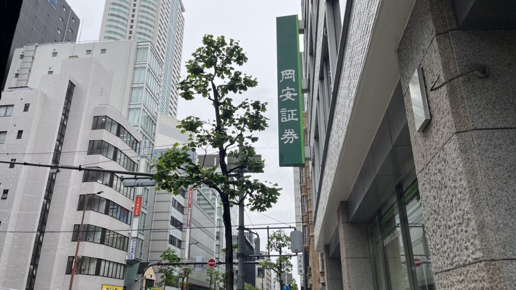 岡安証券の看板が掲げられたビルを空に向いて撮った写真